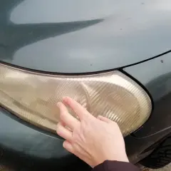 Dłoń dotyka pożółkłej lampy samochodowej, sugerując czyszczenie lamp samochodowych WD-40.