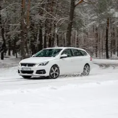 Białe kombi na zakręcie leśnej drogi. Nawet z oponami letnimi na śniegu, auto dzielnie pokonuje zimowe warunki.