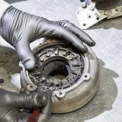 Ręce w rękawiczkach naprawiają nieszczelną turbinę spaliny, czyszcząc mechanizm zmiennej geometrii.