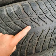 Dłoń wskazuje na minimalny bieżnik opony letniej, który jest mocno zużyty.