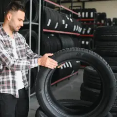 Mężczyzna w kratę ogląda nową oponę, zastanawiając się, czy nowe opony muszą się ułożyć. W tle widać regały pełne opon.