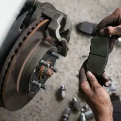 Mechanik trzyma nowe klocki hamulcowe, obok zardzewiała tarcza hamulcowa i narzędzia.