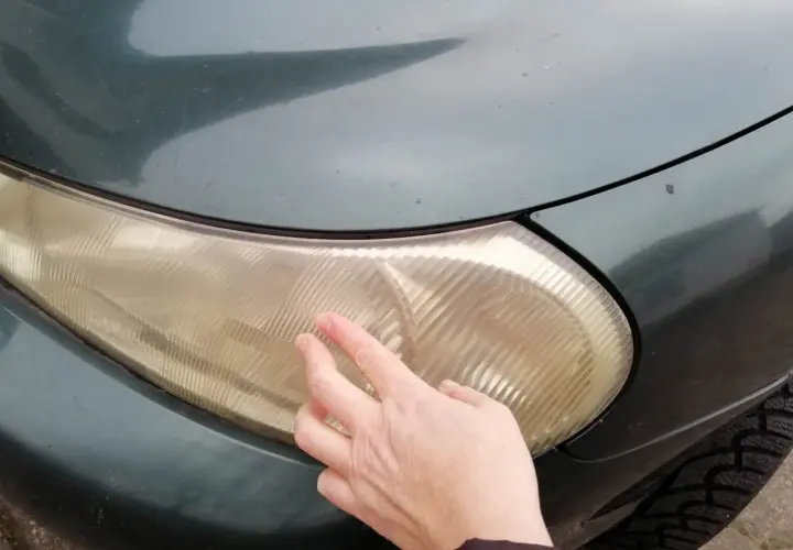 Dłoń dotyka pożółkłej lampy samochodowej, sugerując czyszczenie lamp samochodowych WD-40.