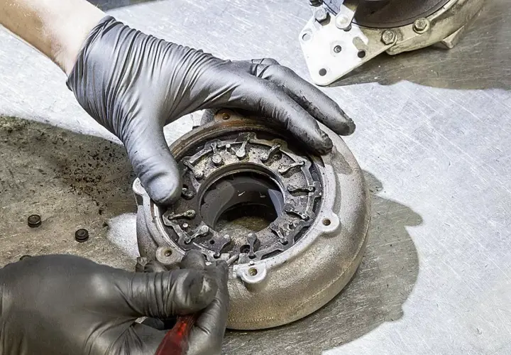 Ręce w rękawiczkach naprawiają nieszczelną turbinę spaliny, czyszcząc mechanizm zmiennej geometrii.