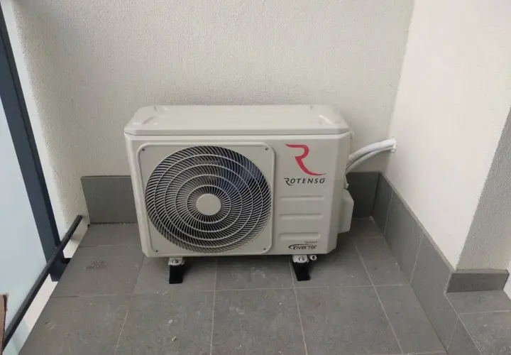Jednostka zewnętrzna klimatyzacji Rotenso z logo, zamontowana na balkonie. Złącze klimatyzacji jest widoczne po prawej stronie.