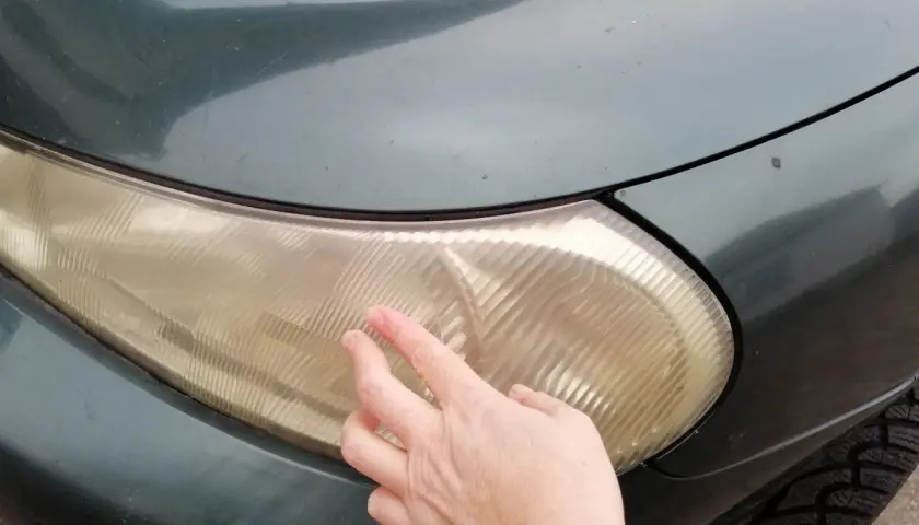 Dłoń dotyka pożółkłej lampy samochodowej, sugerując czyszczenie lamp samochodowych WD-40.