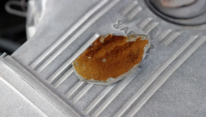 Fragment metalowej obudowy, prawdopodobnie lekko przytarty silnik, z widocznym fragmentem rdzy lub nalotu.