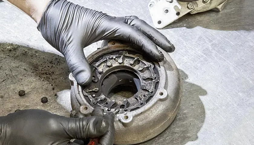 Ręce w rękawiczkach naprawiają nieszczelną turbinę spaliny, czyszcząc mechanizm zmiennej geometrii.