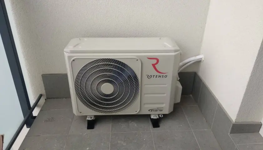 Jednostka zewnętrzna klimatyzacji Rotenso z logo, zamontowana na balkonie. Złącze klimatyzacji jest widoczne po prawej stronie.