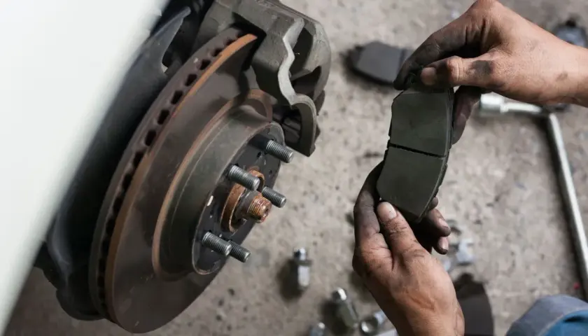 Mechanik trzyma nowe klocki hamulcowe, obok zardzewiała tarcza hamulcowa i narzędzia.