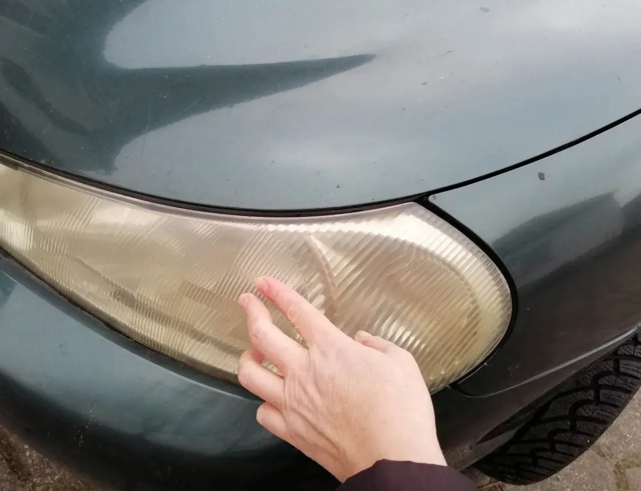 Dłoń dotyka pożółkłej lampy samochodowej, sugerując czyszczenie lamp samochodowych WD-40.