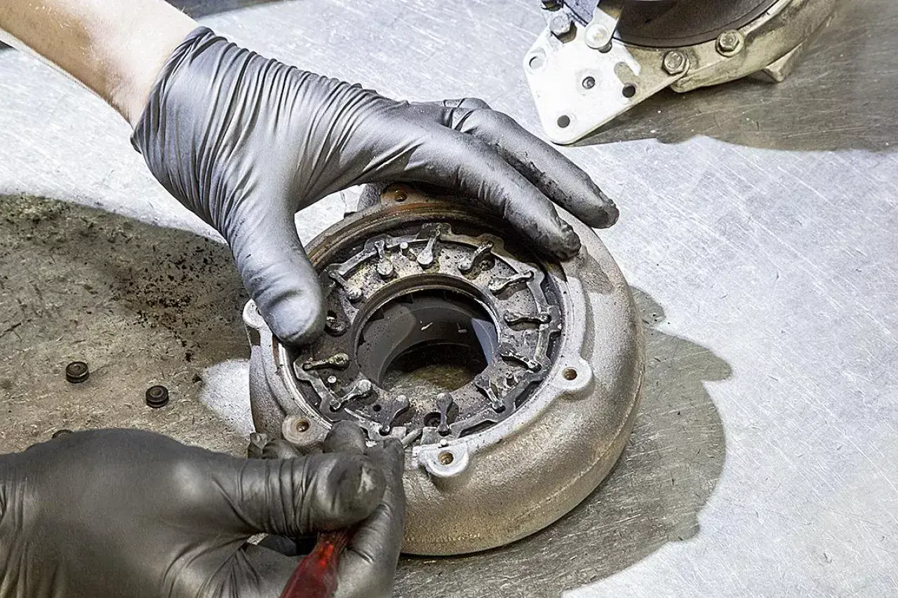 Ręce w rękawiczkach naprawiają nieszczelną turbinę spaliny, czyszcząc mechanizm zmiennej geometrii.