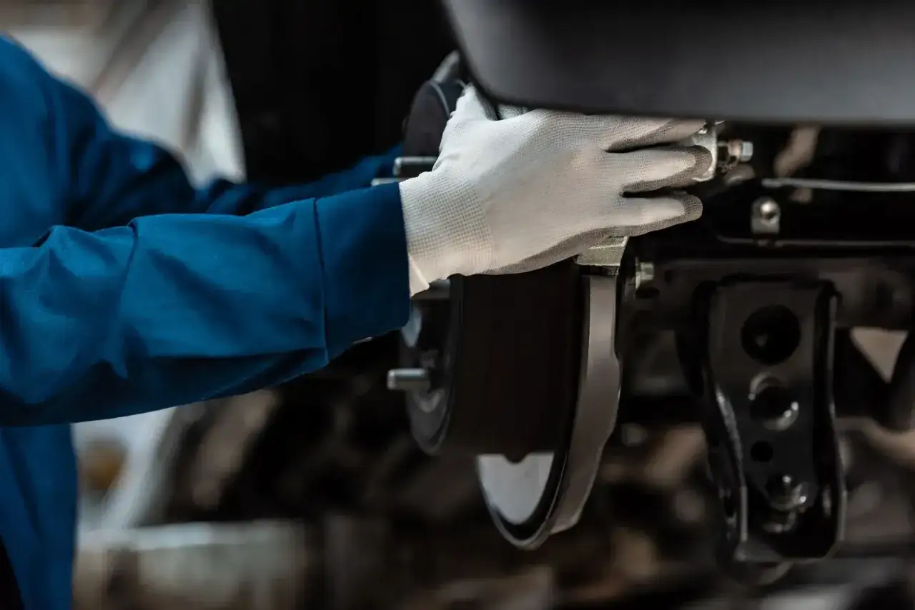 Mechanik w białej rękawiczce wymienia klocki hamulcowe i tarcze. Czas pracy zależy od modelu auta.